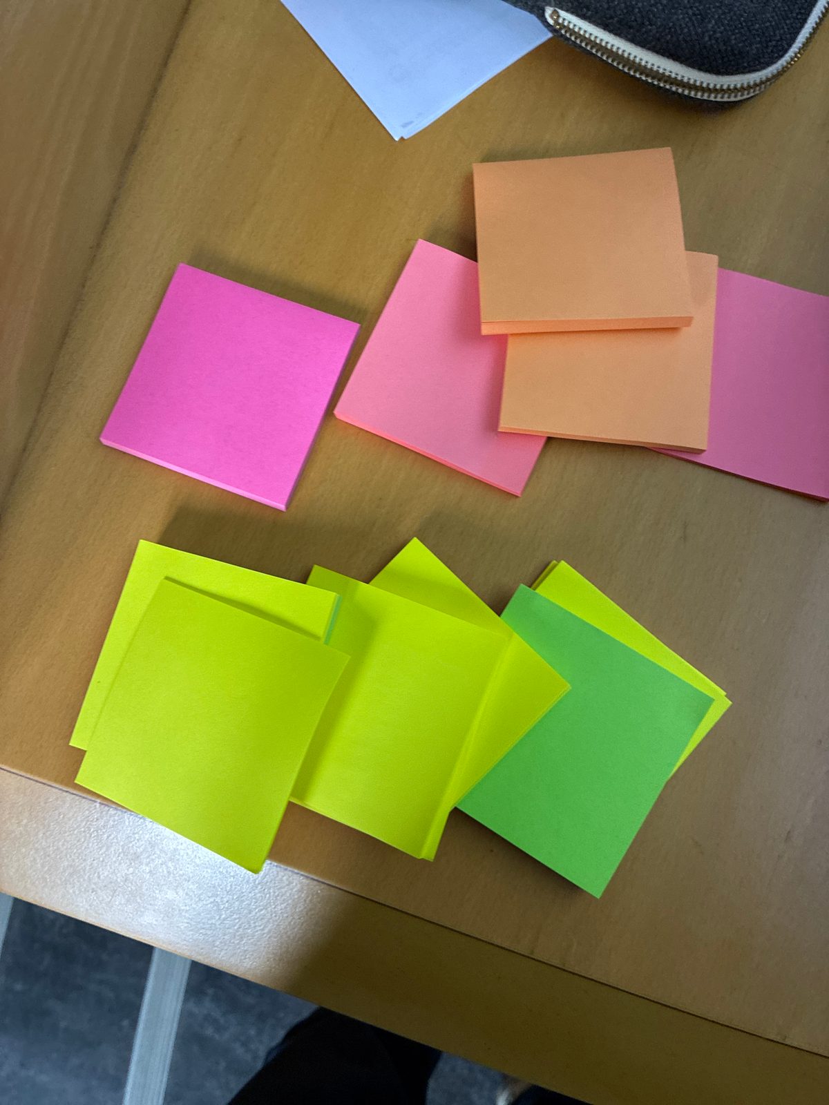 Photo de deux familles de post-it posés sur une table en bois : à gauche, des post-it roses et orange ; à droite, des post-it verts et jaunes.
